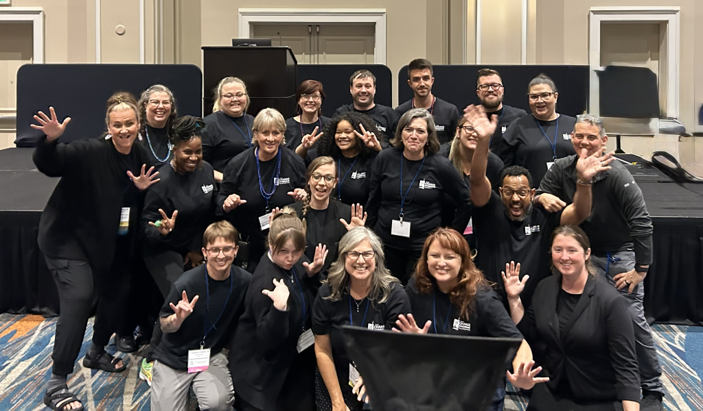 Group of interpreters posing at the CHARGE Syndrome Foundation conference, wearing black logo shirts and badges.