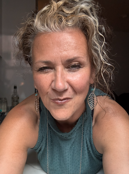 Susie Morgan smiling indoors, wearing teal top and earrings.