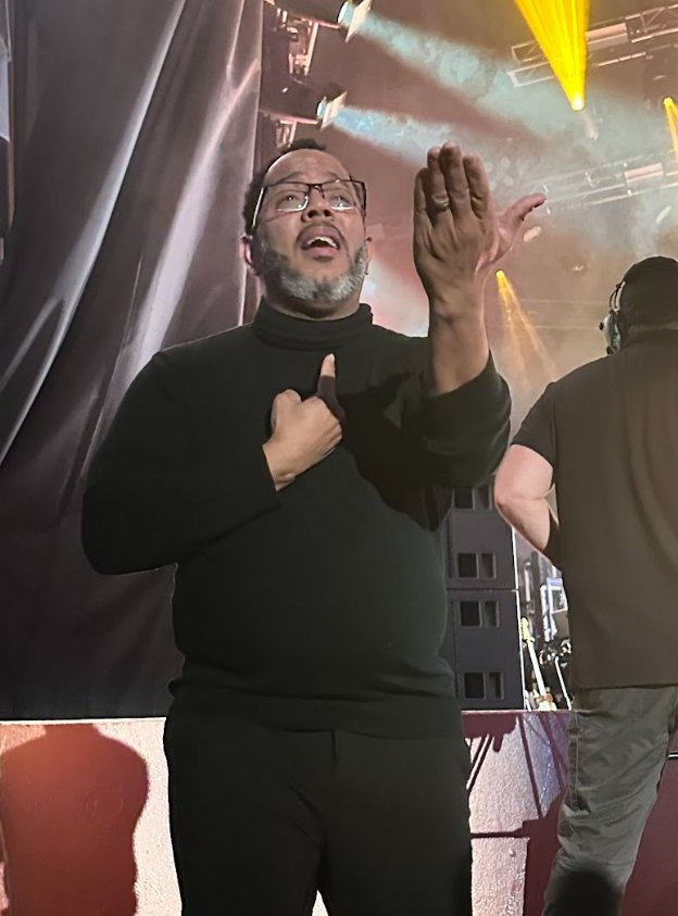 Carmelo, a sign language interpreter, signing on stage at a live concert.