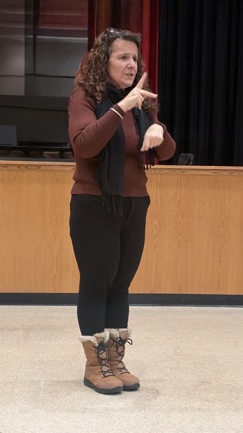 An interpreter signing in ASL in a school auditorium, standing in front of the stage.
