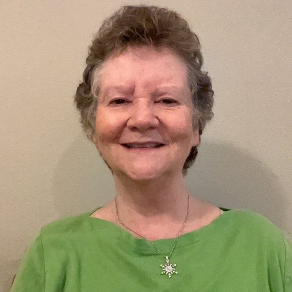 Jamie Pope smiling, wearing a green top and a snowflake pendant necklace.