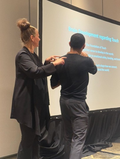 A presenter communicating through touch on a man's back during a conference session on touch and brain development.